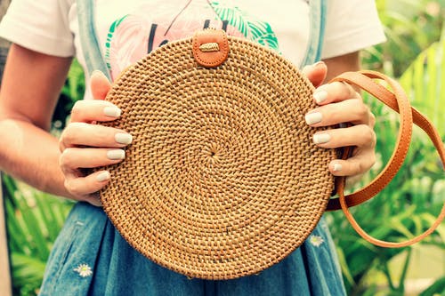 女人拿着一个圆形的棕色藤制手提袋的特写照片 · 免费素材图片
