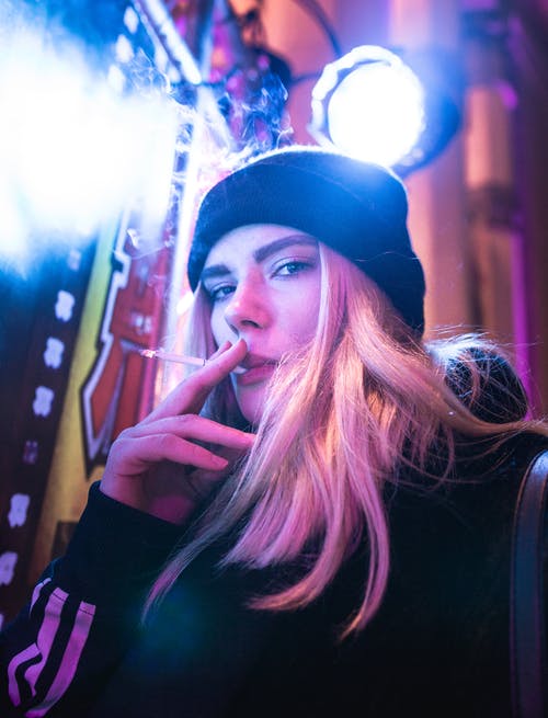 在明亮的灯光下抽烟的无檐小便帽的女人的肖像照片 · 免费素材图片