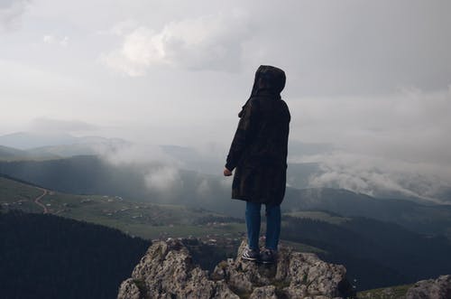 身穿黑色外套站在山边的人 · 免费素材图片