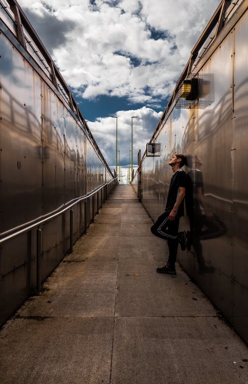 一个男人穿着黑色t恤和裤子倚在墙上的街拍 · 免费素材图片