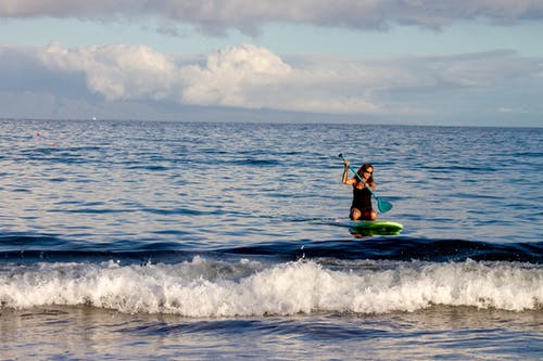女人骑绿色冲浪板使用桨 · 免费素材图片