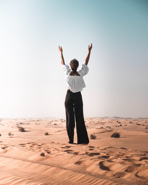 后视图的女人，她举起手来站在沙漠的沙滩上的照片 · 免费素材图片
