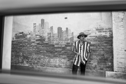 男子倚在砖墙上的单色照片 · 免费素材图片