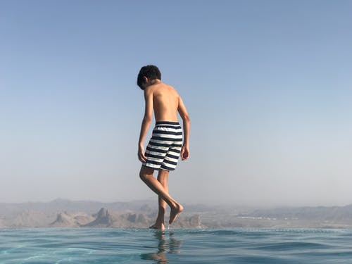 后视图的男孩穿着泳裤站在无边泳池的边缘 · 免费素材图片