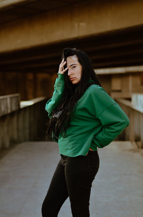 美丽的女人，在绿色的运动衫和黑色的裤子，摆在混凝土通路中间的白癜风的侧面照片 · 免费素材图片