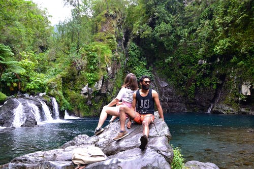 夫妻坐在水体附近的岩石上 · 免费素材图片