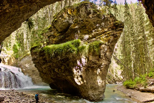 女人站在瀑布和巨大的岩层附近 · 免费素材图片