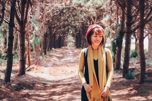 沿树间步道独自行走的微笑妇女的照片 · 免费素材图片