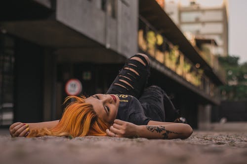 一个女人躺在建筑物附近的背上的照片 · 免费素材图片