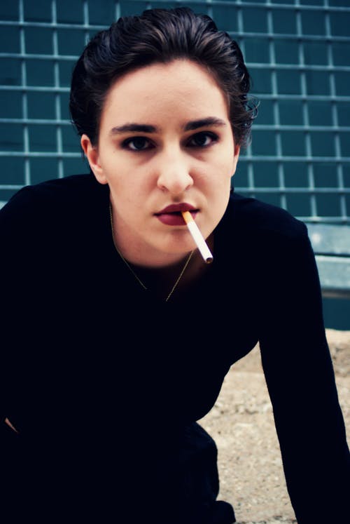 摆在嘴里的香烟摆姿势的黑色运动衫的女人的照片 · 免费素材图片