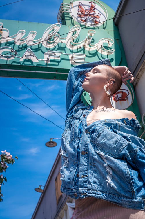 低角度的咖啡厅招牌下摆姿势的蓝色牛仔夹克的女人的照片 · 免费素材图片