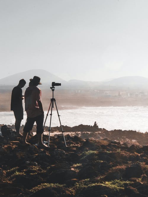 两名男子站在岩石上拍照水的身体 · 免费素材图片