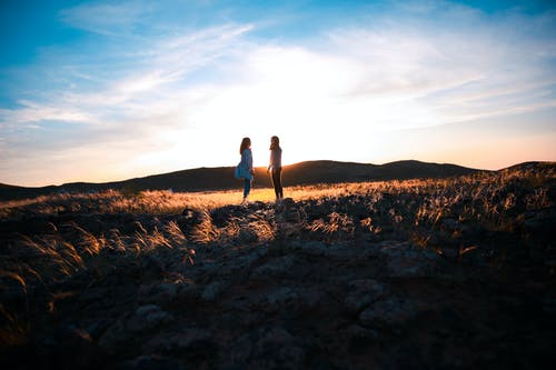两个女人站在棕色的草田 · 免费素材图片