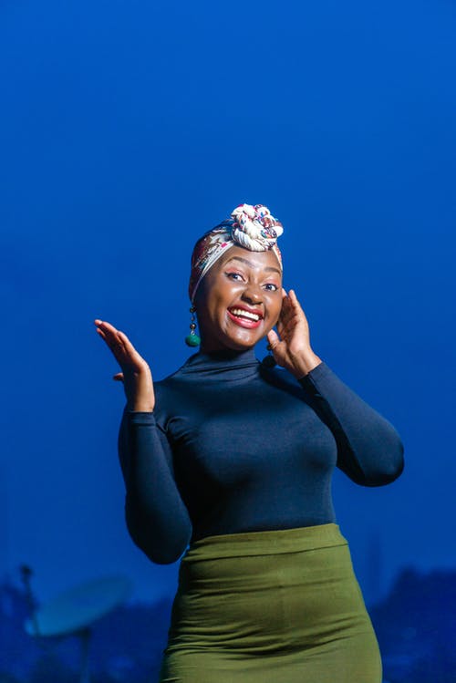 蓝色长袖的上衣和绿色的裙子，摆在蓝色背景下的微笑女人的照片 · 免费素材图片