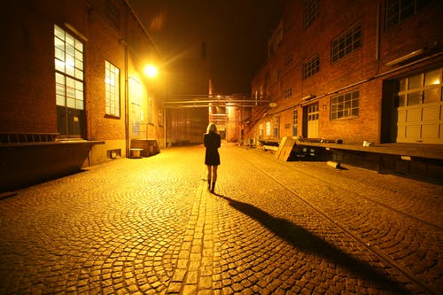 女人独自一人走在鹅卵石巷子里在晚上的背影照片 · 免费素材图片