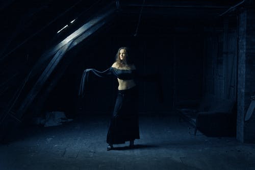 穿着黑色衣服的女人站在黑暗的废弃建筑摆姿势，看着别处的照片 · 免费素材图片