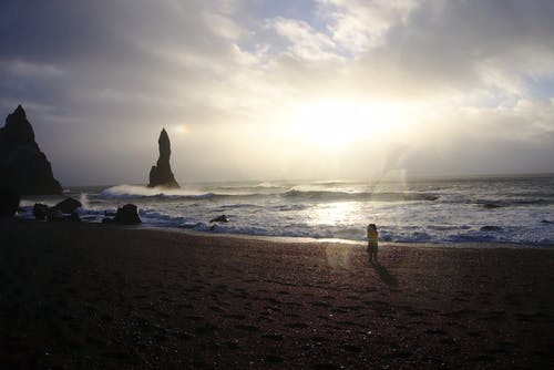 独自站在海滩看着地平线的年轻女孩的背影照片 · 免费素材图片