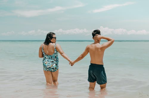 夫妇在游泳服装握着的手，而站在水中在海滩后视图 · 免费素材图片