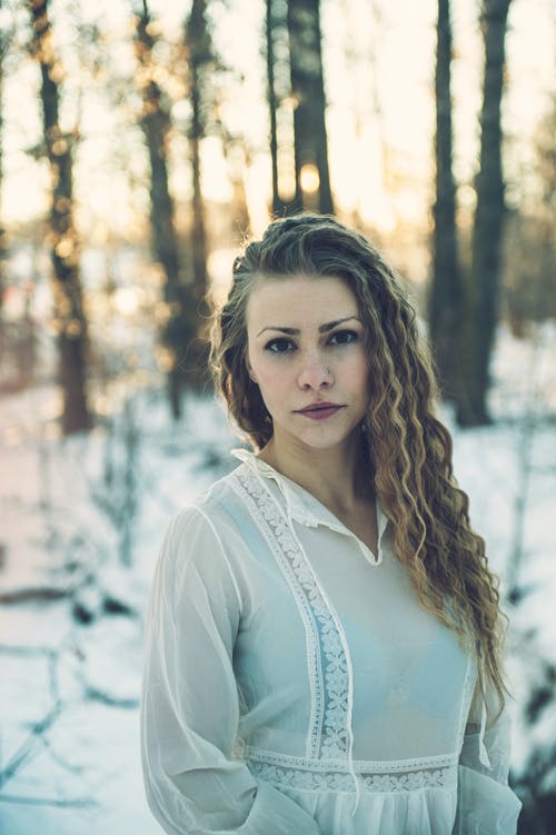 女人穿着白裙子站在雪地里的选择性焦点照片 · 免费素材图片