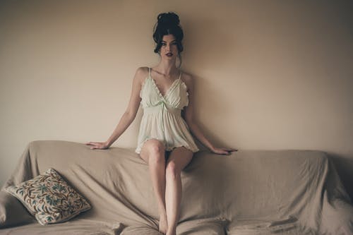 美丽的女人，穿着白色的晚礼服，坐在沙发靠背上的照片 · 免费素材图片