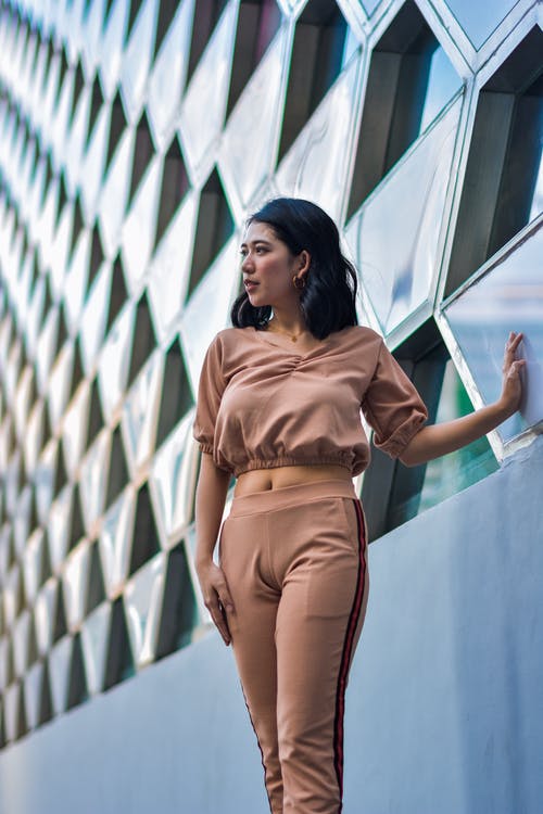 女人站在棕色的作物顶部和她的手掌在建筑物上的裤子的照片 · 免费素材图片