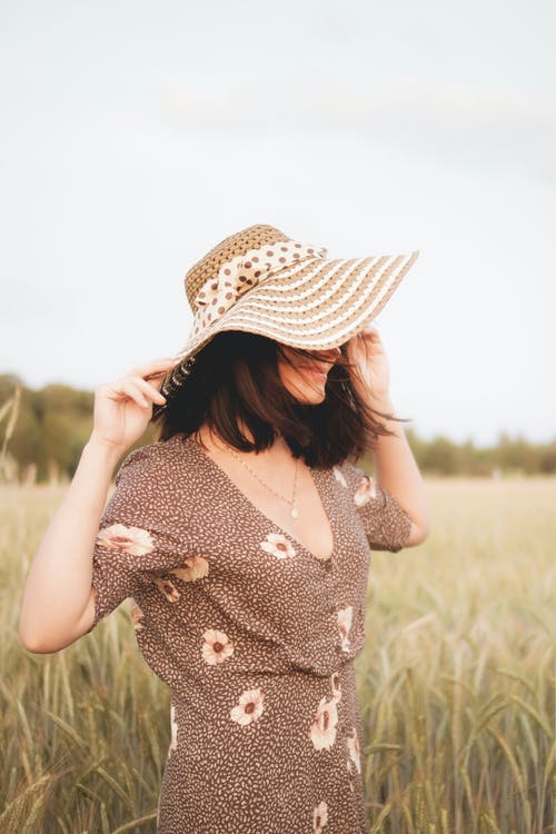 女人穿着花裙子和遮阳帽站在草地上的侧视图照片 · 免费素材图片