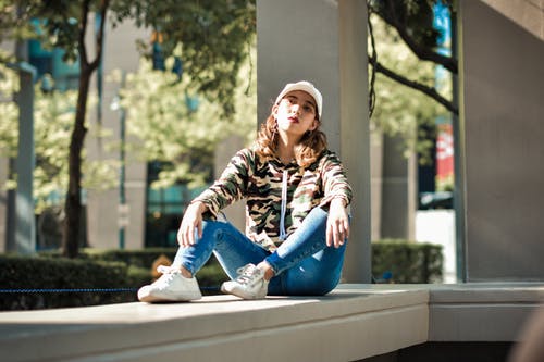 一个女人坐在白色混凝土上的选择性焦点摄影 · 免费素材图片