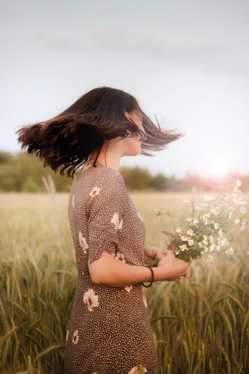 一个女人穿着棕色花裙，拿着白花的浅焦点照片 · 免费素材图片