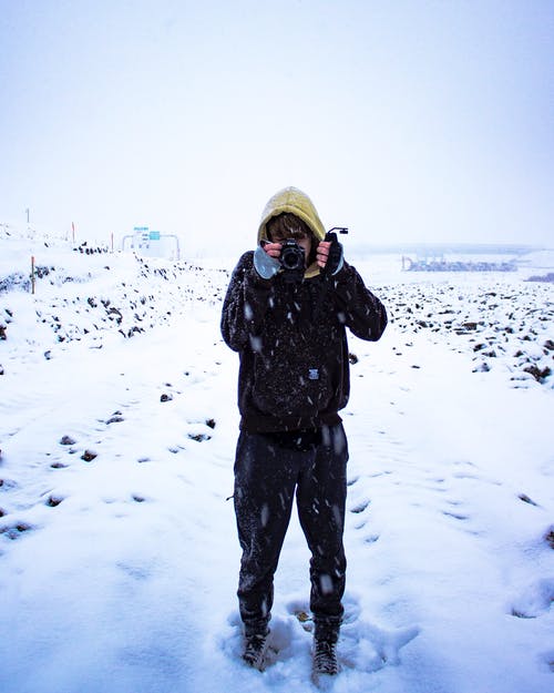 一个人在积雪的地面上拿着照相机的照片 · 免费素材图片