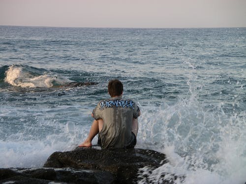男子坐在岩石和水溅 · 免费素材图片