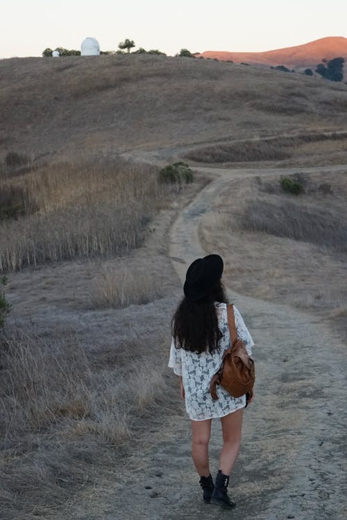 妇女走在土路上，背着棕色袋子的后视图照片 · 免费素材图片