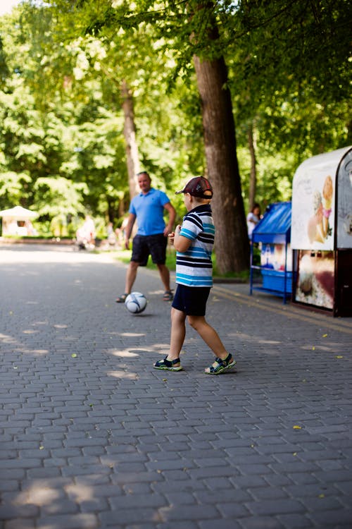 男孩和男人在人行道上踢足球 · 免费素材图片