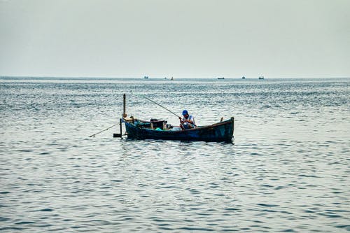 男子坐在渔船上平静的水体 · 免费素材图片