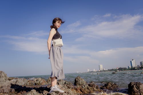 女人站在水边的岩石上的照片 · 免费素材图片