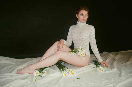 女人穿着白色钩针编织紧身衣坐在棕色的地毯，用鲜花 · 免费素材图片