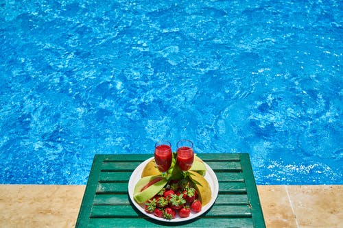 两杯饮料和水果盘在游泳池旁 · 免费素材图片