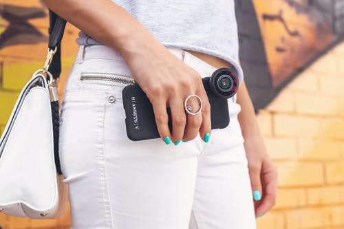 女人穿着灰色衬衫和白色牛仔牛仔裤，拿着黑色的智能手机 · 免费素材图片