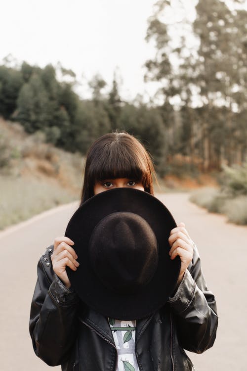 女人用软呢帽遮住脸的一部分时站在路中间的选择性聚焦照片 · 免费素材图片