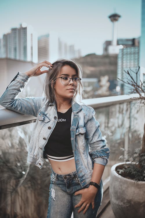 穿蓝色牛仔夹克的女人斜倚在不锈钢栏杆 · 免费素材图片