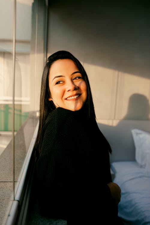 黑色毛衣站在玻璃窗口的微笑妇女 · 免费素材图片