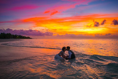 男人和女人在日落期间在海洋中接吻 · 免费素材图片