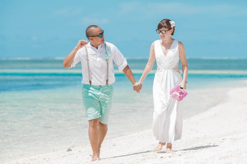 新娘和新郎在海边散步时手牵着手 · 免费素材图片