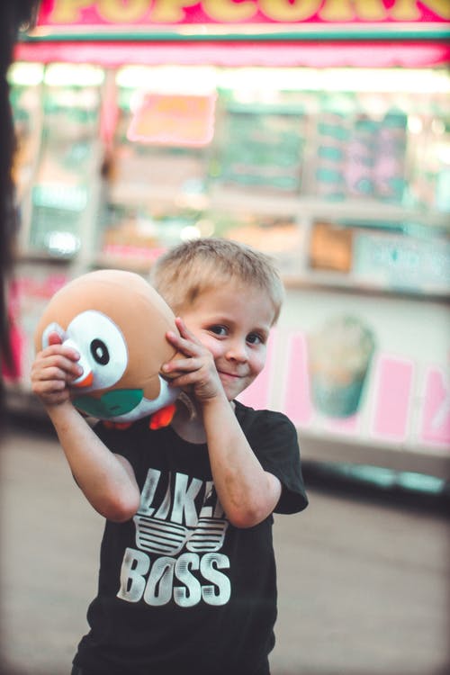 微笑的男孩抱着棕色毛绒玩具的选择性焦点照片 · 免费素材图片