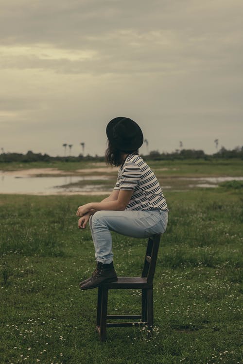 女人坐在草地中间看着别处的棕色木椅上的照片 · 免费素材图片