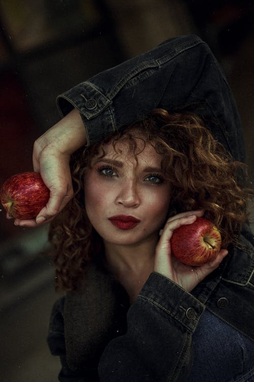 穿蓝色牛仔夹克与两个红苹果合影的女人的照片 · 免费素材图片