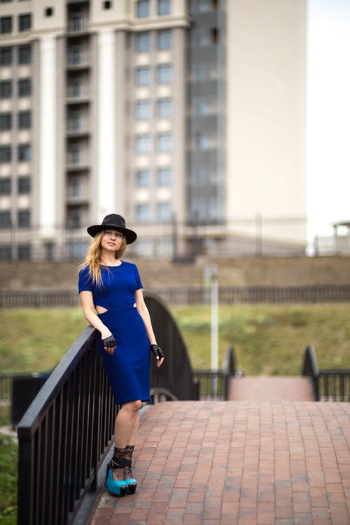 一名妇女的选择聚焦照片蓝色礼服的和倾斜在金属栏杆的帽子 · 免费素材图片