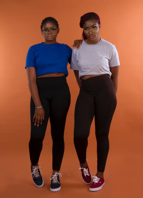 两个女人穿着绑腿和t恤摆在橙色背景前的照片 · 免费素材图片