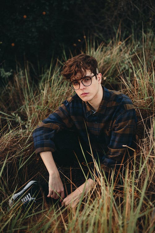 男人穿着蓝色和棕色的格子运动衫，坐在草地上 · 免费素材图片