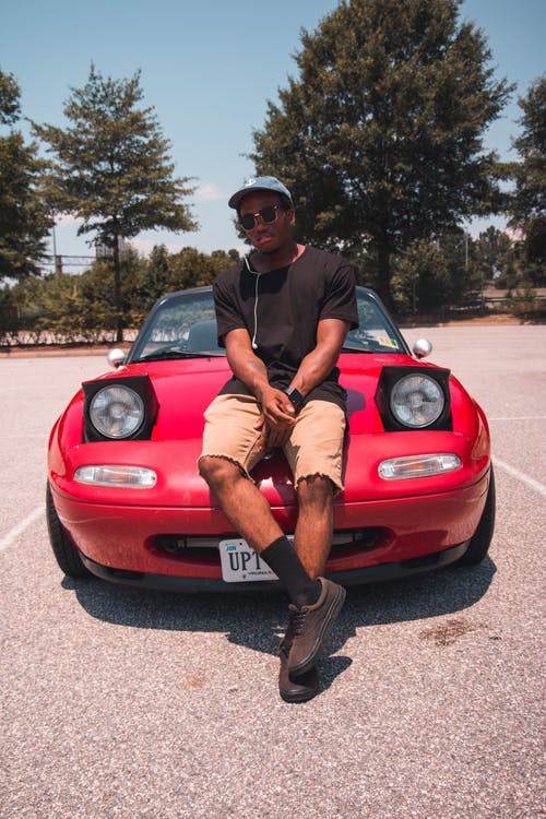 一个男人穿着黑色衬衫，坐在红色汽车引擎盖上的照片 · 免费素材图片