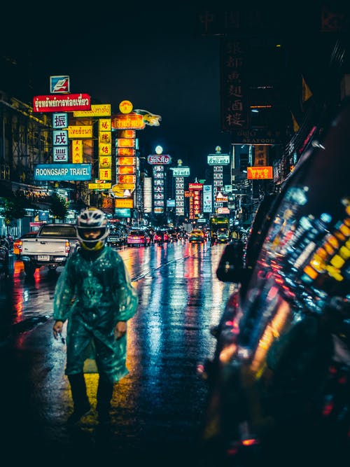 穿着绿色雨衣和白色全盔站在湿街中间的男人 · 免费素材图片